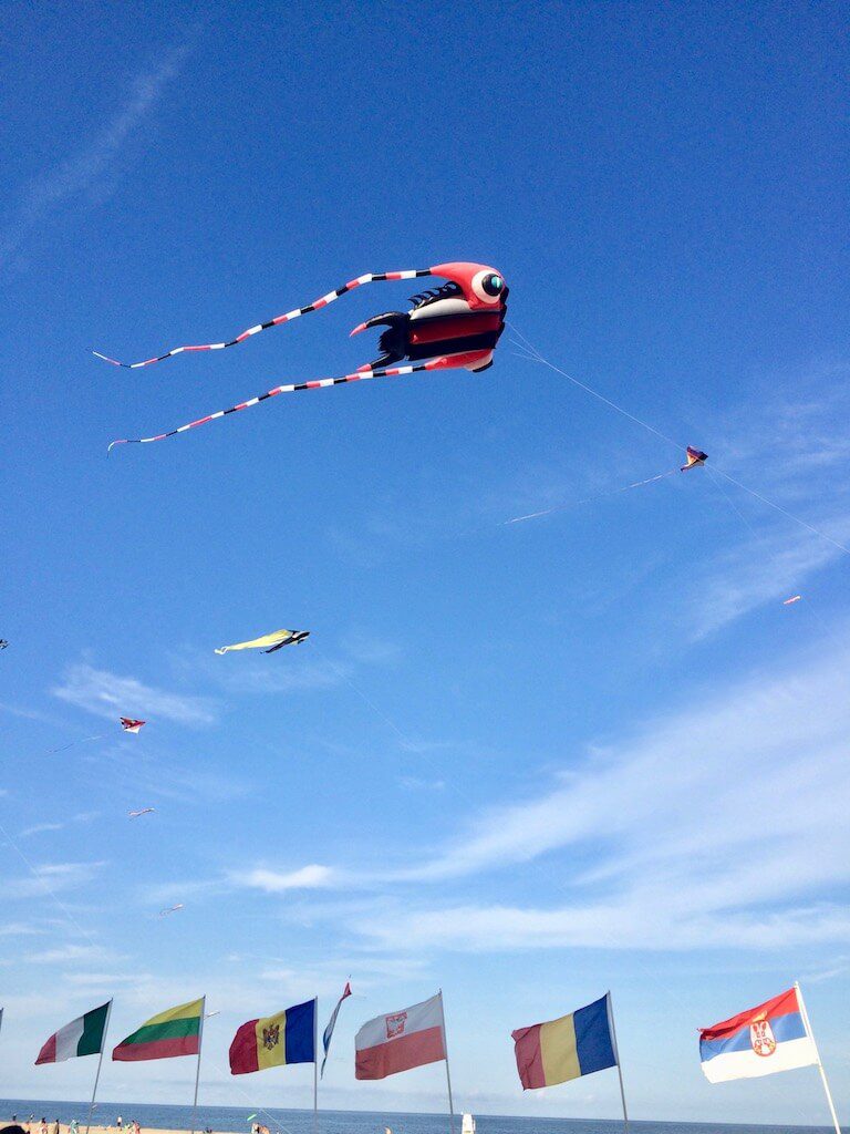 four kites fly in the blue sky over a row of flags waving in the breeze - fun things to do in ocean city md