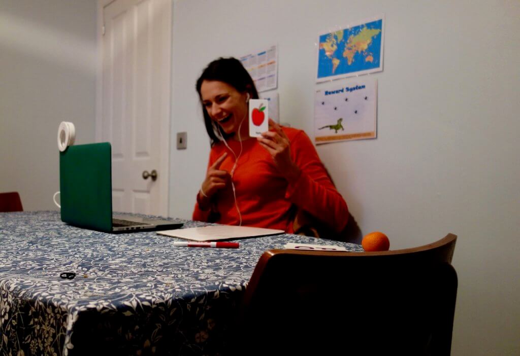 Nicola in an orange shirt teaching to the computer, holding a flash card and smiling