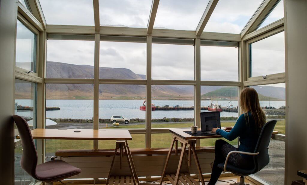 woman sitting at a desk looking out over a beautiful landscape while working on a computer.  digital nomad jobs