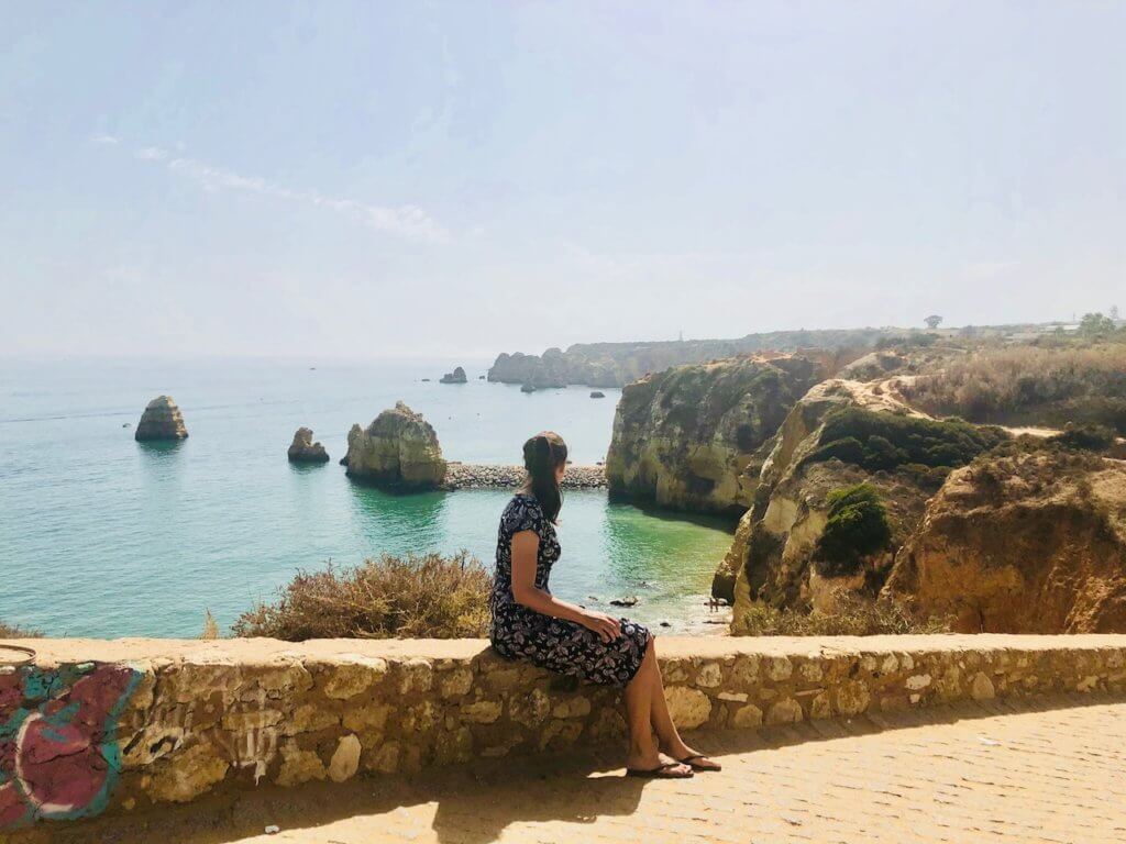 Nicola sitting on a stone wall looking out over the cliffs in Portugal