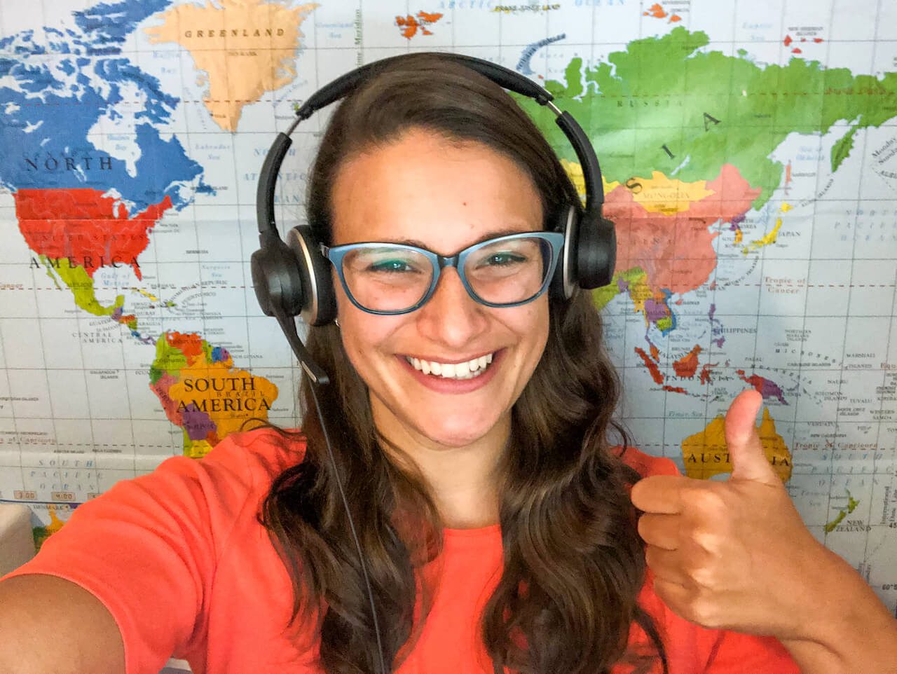 equipment for teaching online teacher in an orange shirt smiling while wearing a headset in front of a world map