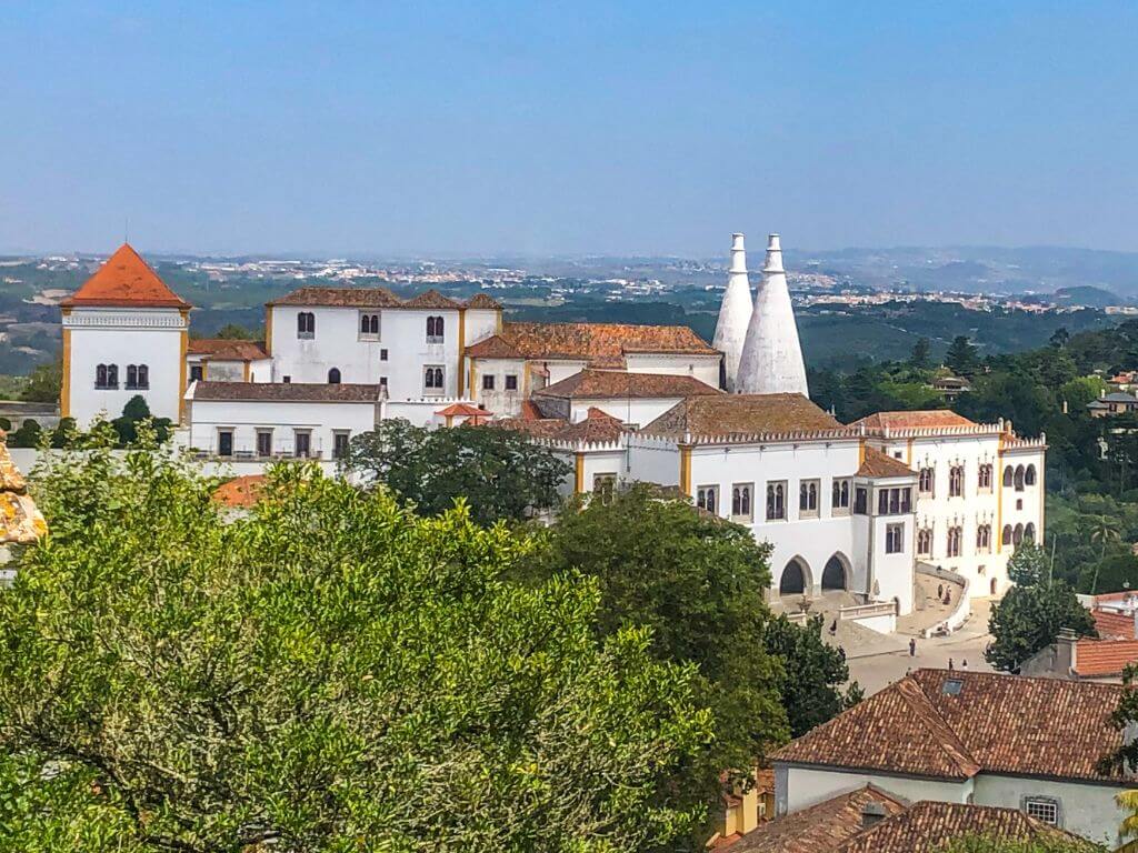 Full view of the National Palace of Sintra with white walls, two conical chimneys, and yellow trim